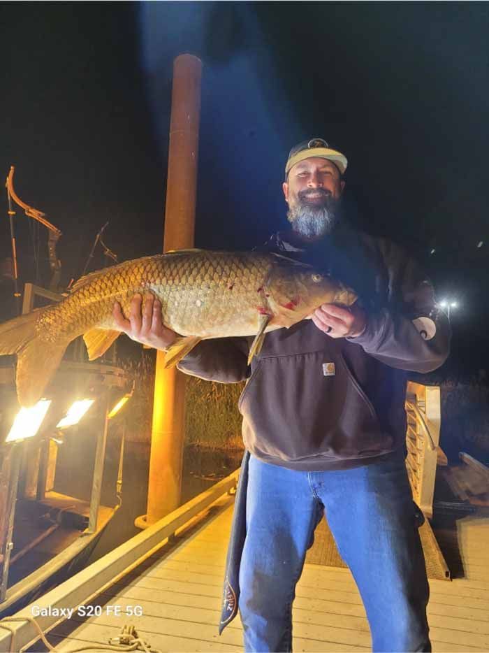 A man with a beard is holding a large fish in his hands.