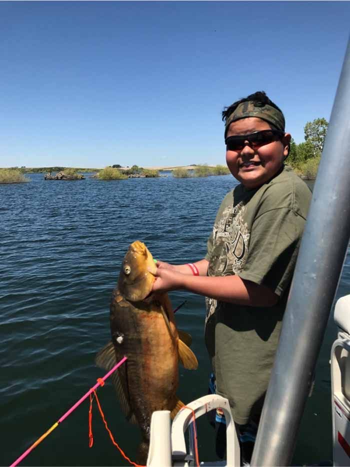 A young boy is holding a large fish on a boat.