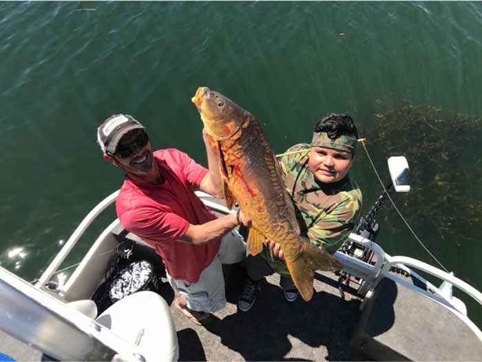 A man and a boy are holding a large fish on a boat.