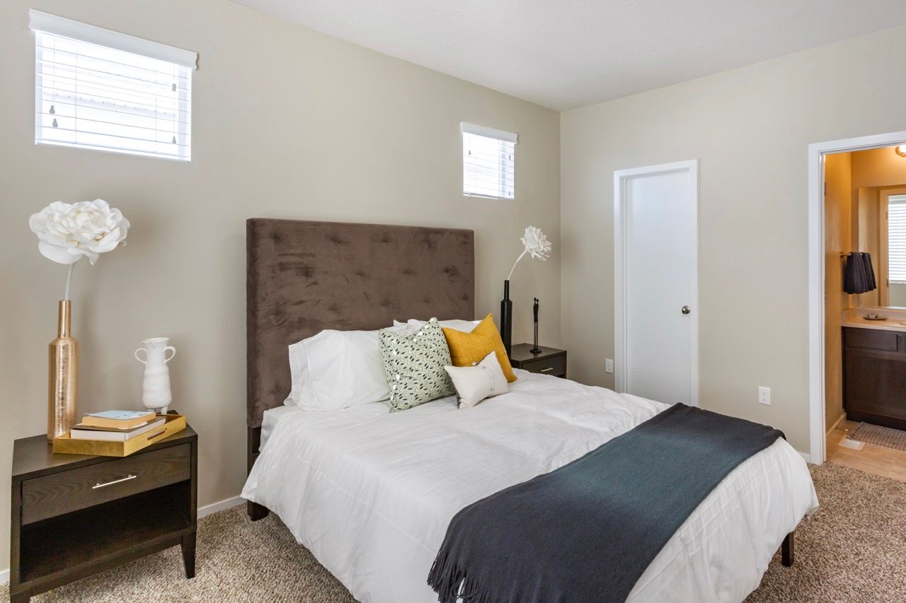 Bedroom with a white bed, brown upholstered headboard, two nightstands, and a bathroom door.