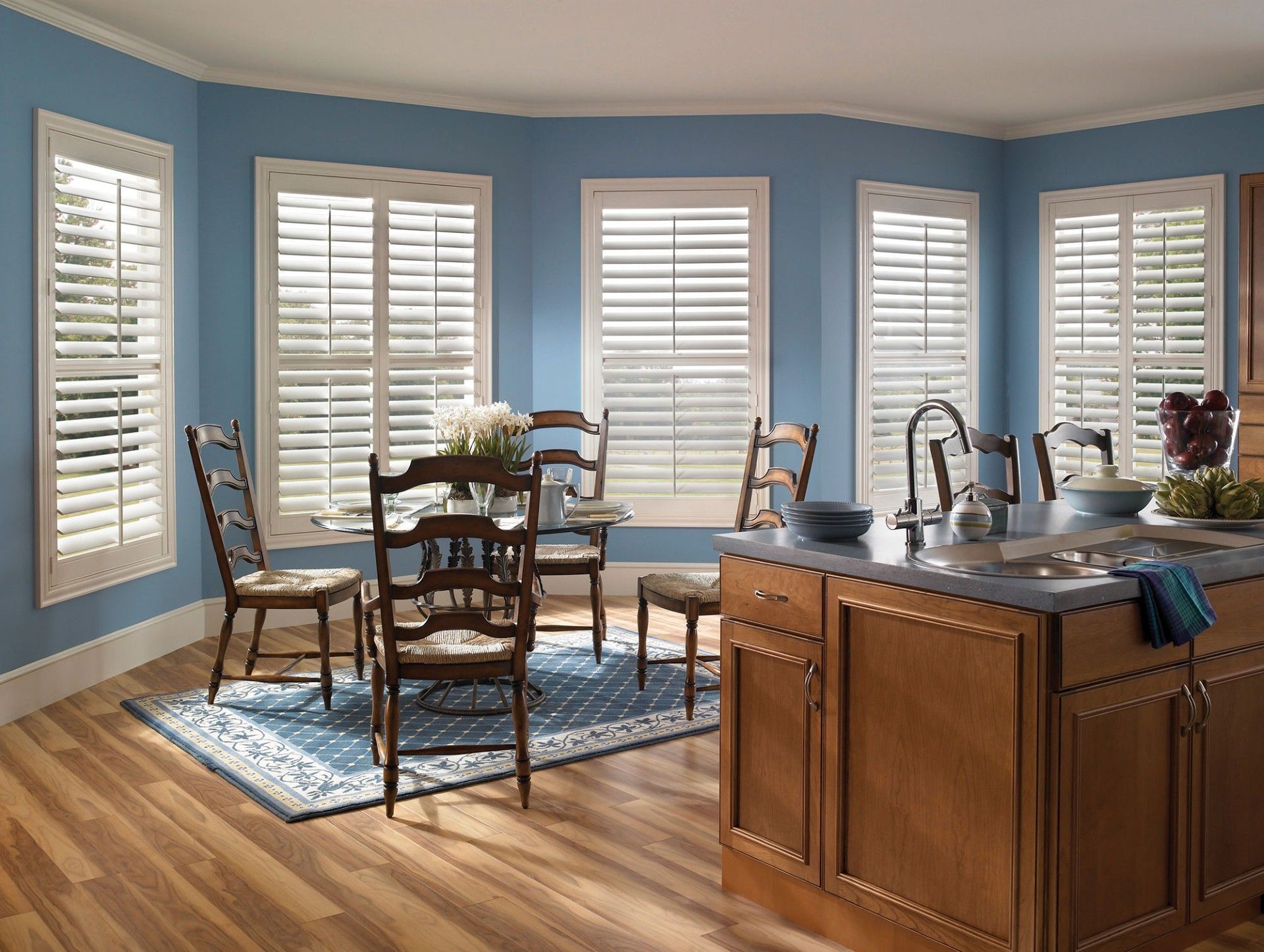 Bright kitchen with blue walls, white shutters, dining table, chairs, and wooden island