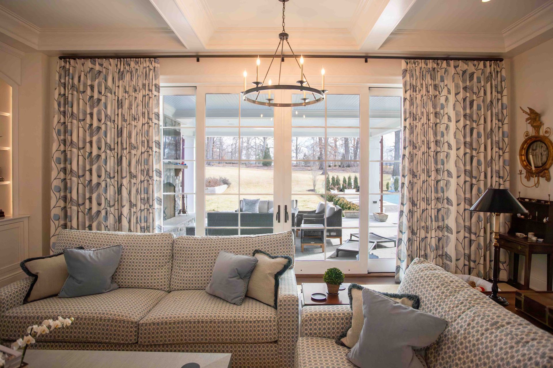 Living room with floral curtains, patterned sofa, French doors opening to a patio and a chandelier.