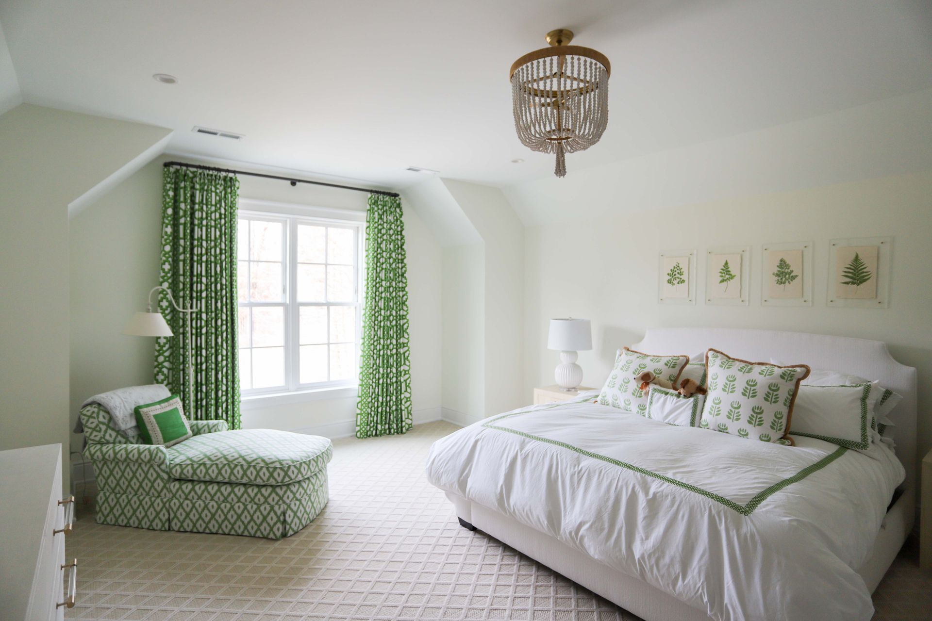 Bedroom with white walls, green patterned curtains and chaise, white bedding, and a decorative light fixture.