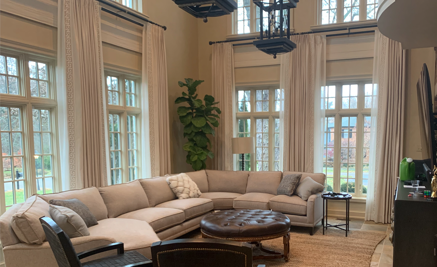 A large, light-colored sectional sofa in a spacious living room with large windows and cream curtains.
