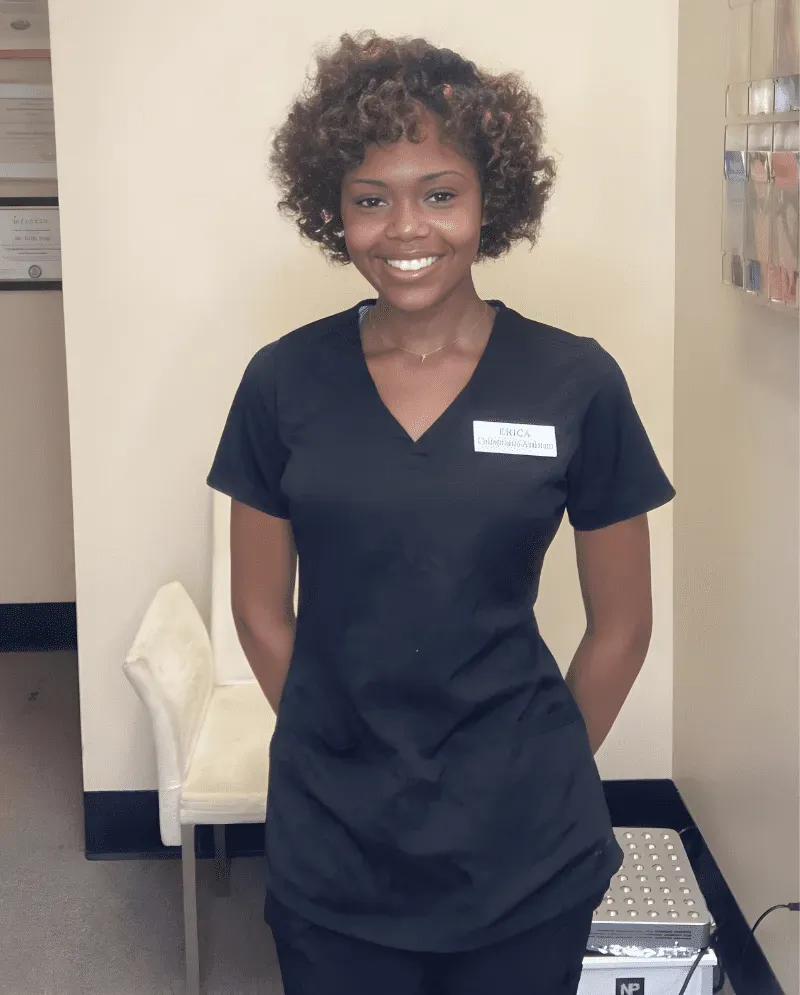 Woman in black v-neck shirt, smiling, hands behind her back, inside a beauty salon.