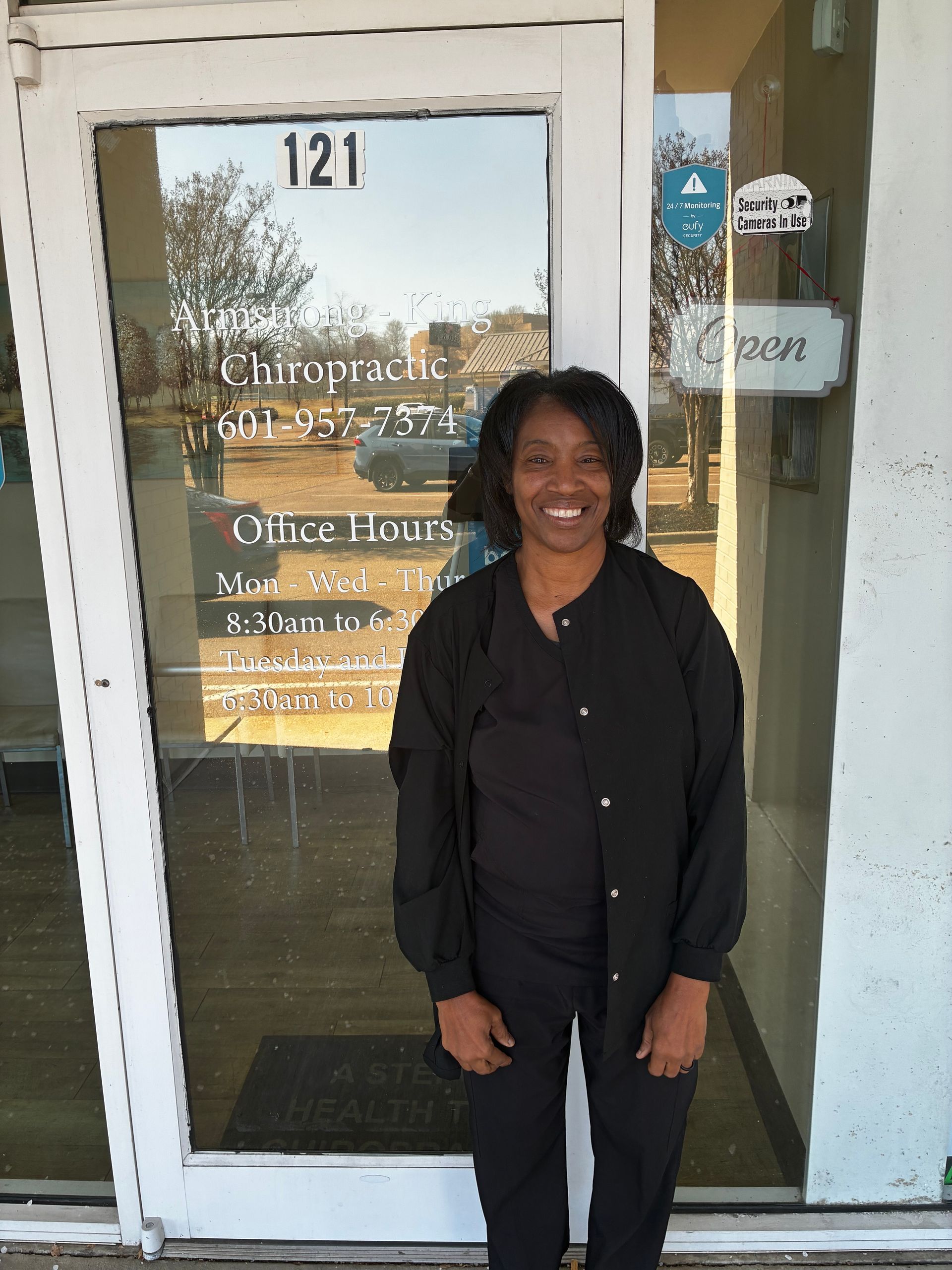 Woman in black v-neck shirt, smiling, hands behind her back, inside a beauty salon.