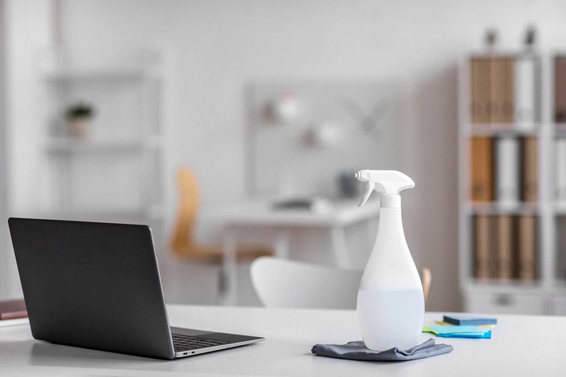 A laptop computer is sitting on a desk next to a spray bottle.