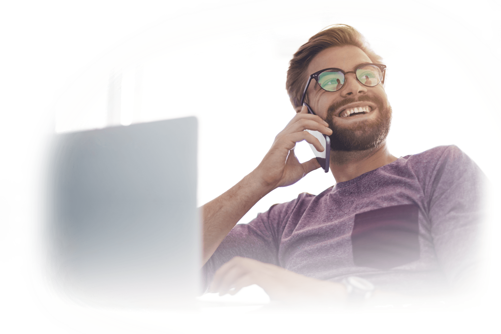 A man is sitting in front of a laptop computer talking on a cell phone.