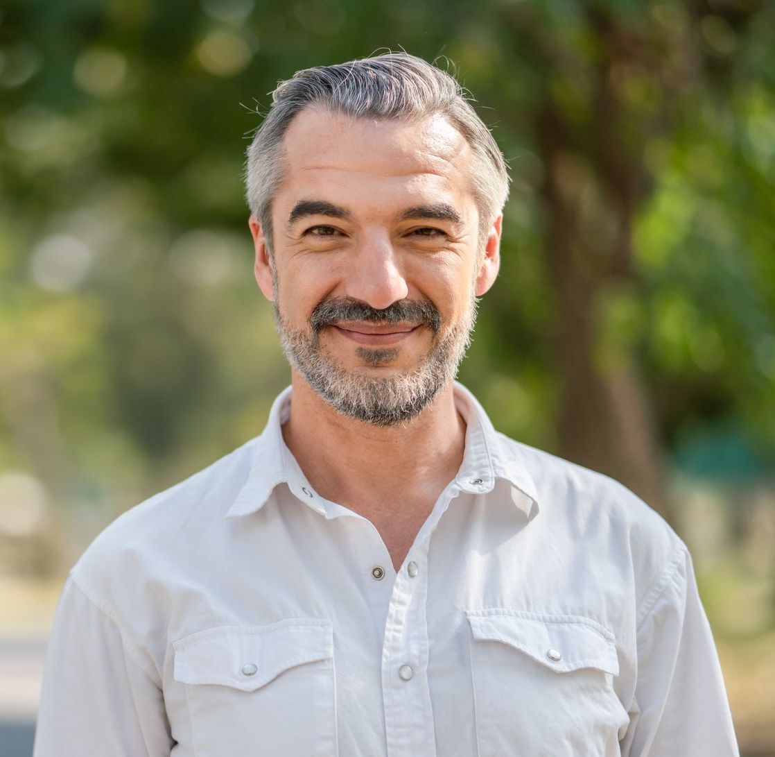 A man with a beard is smiling for the camera while wearing a white shirt.