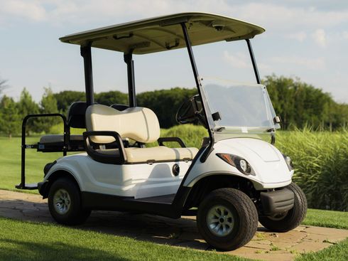 A white golf cart is parked in the grass on a golf course