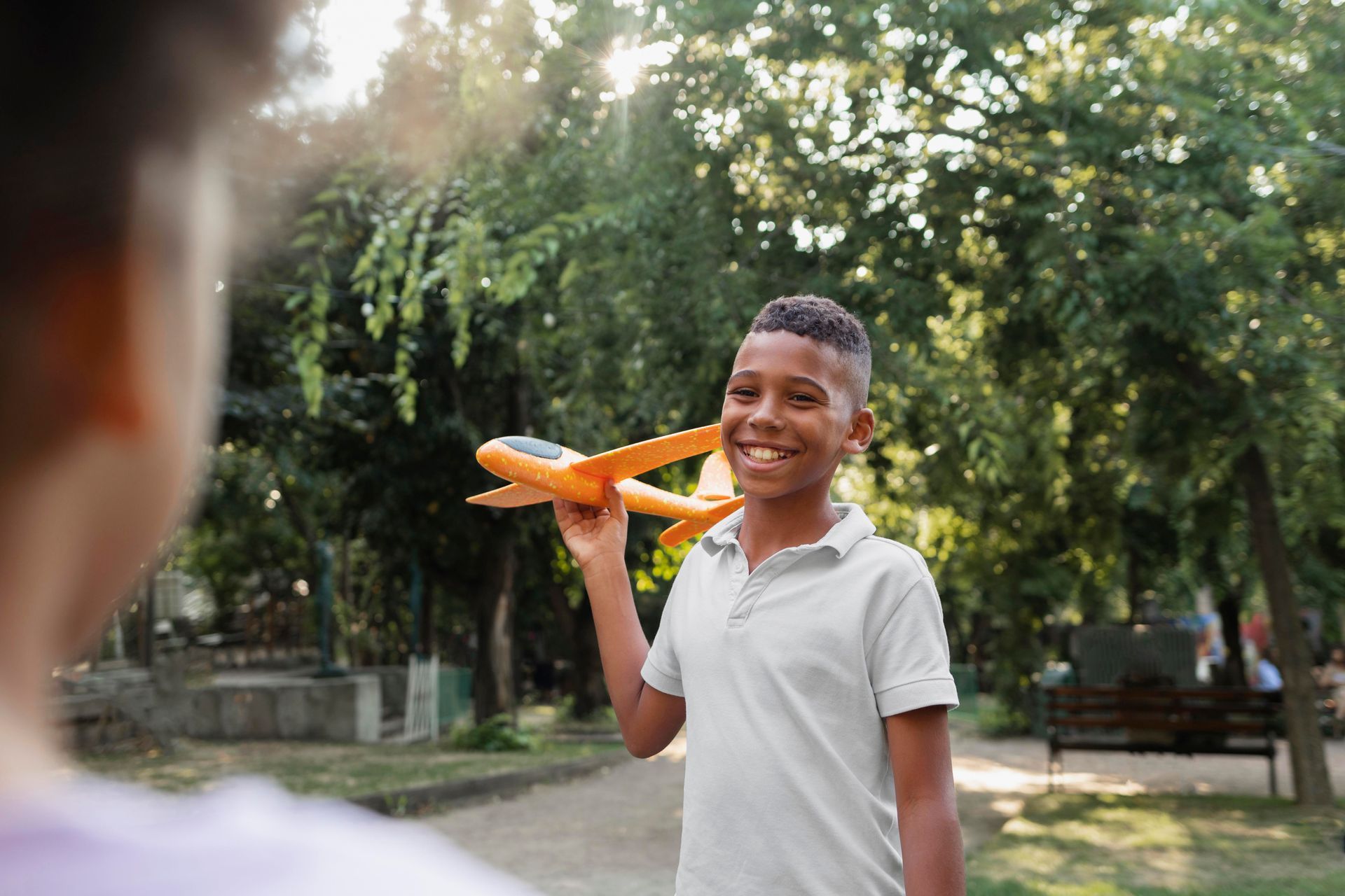 Boy smiling, holding a toy airplane in a park.