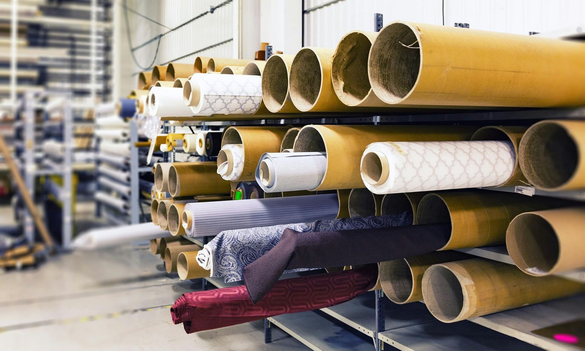 Fabric rolls stored in cardboard tubes on metal shelves in a warehouse.