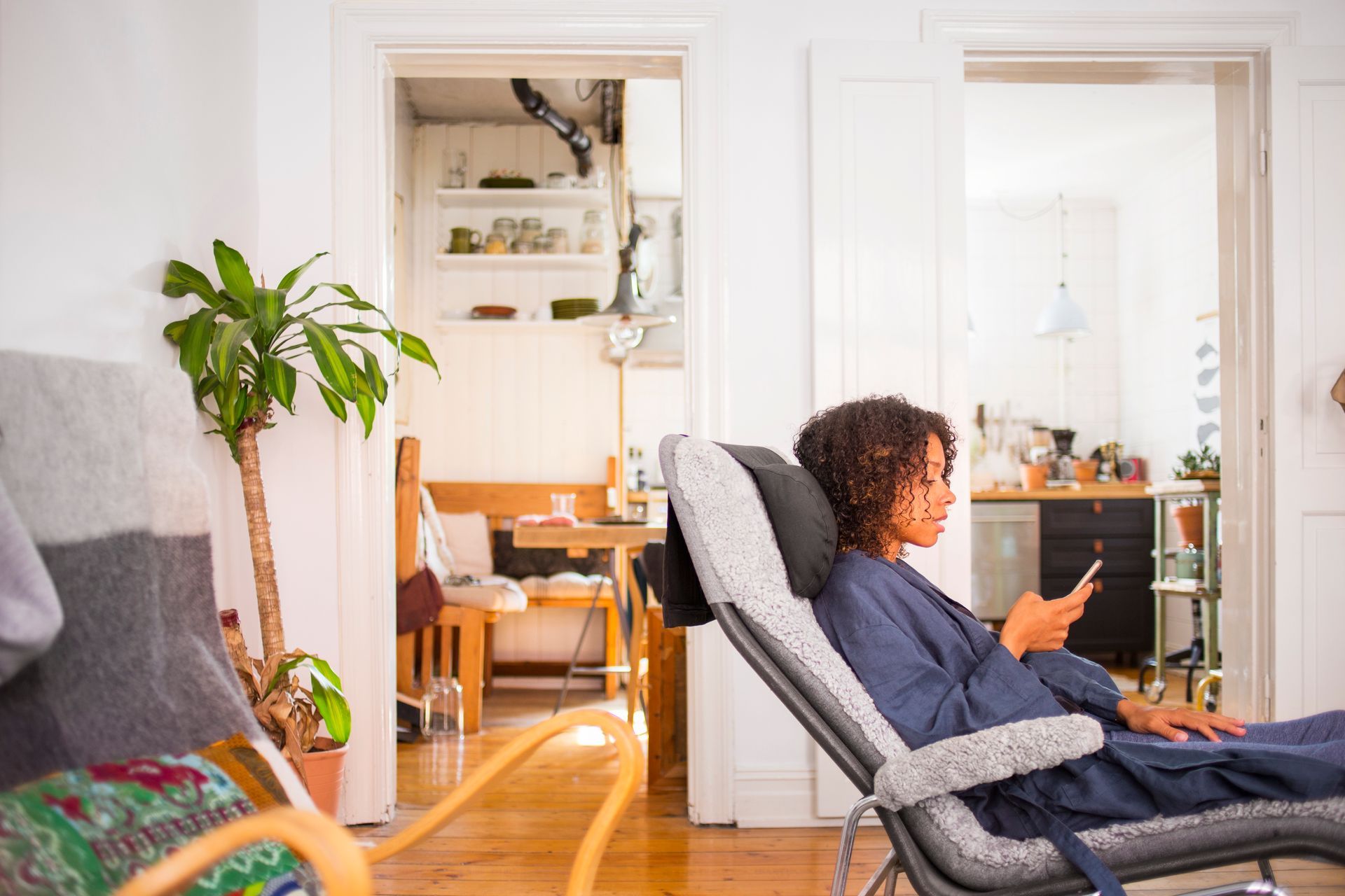 Woman relaxing in a chair, looking at her phone, in a bright living room with a plant.
