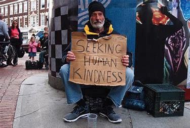 A man is sitting on the sidewalk holding a sign that says seeking human kindness