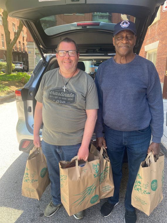 Two men are standing next to each other holding shopping bags in front of a car.