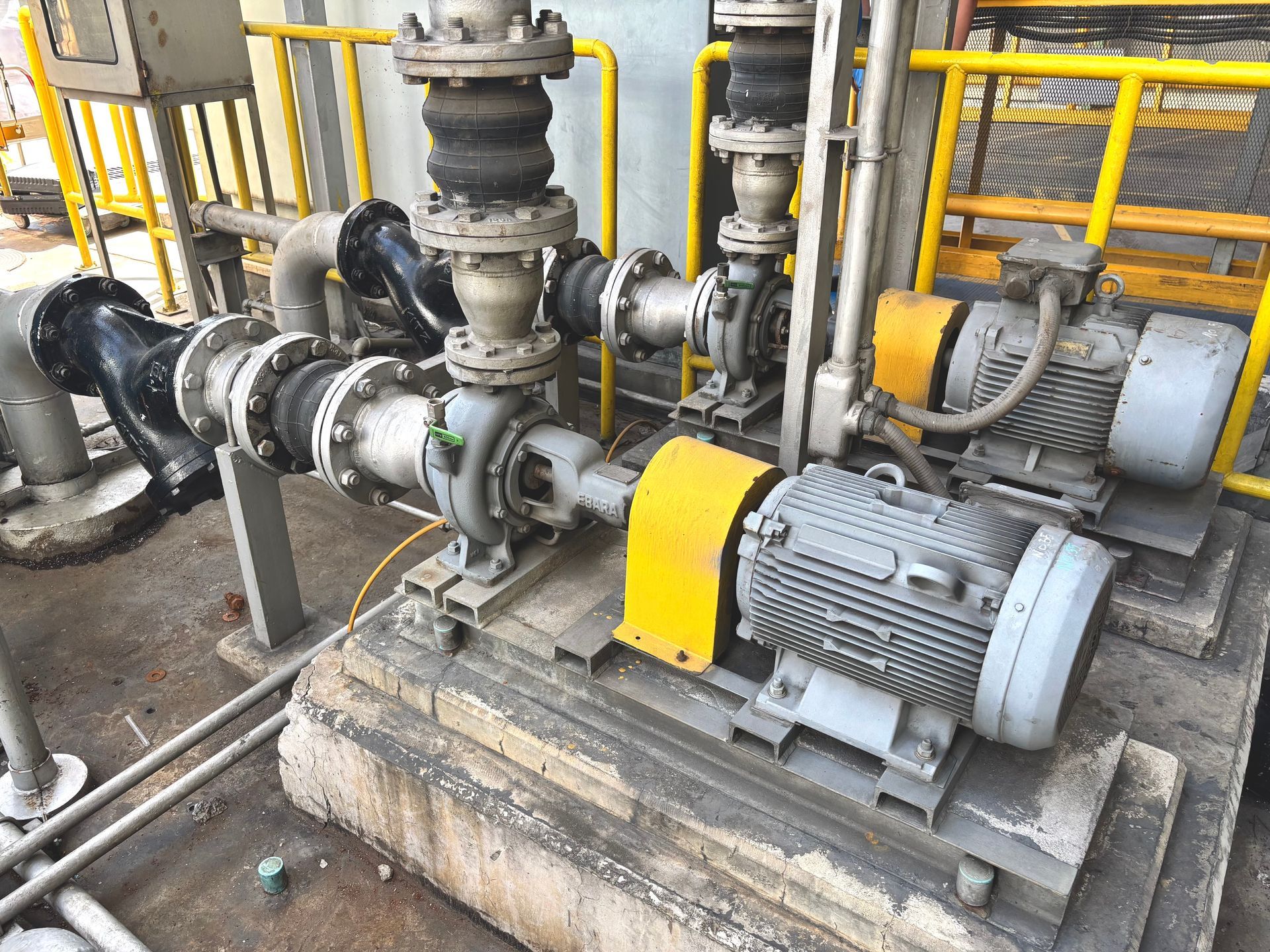 Pumps and motors in an industrial setting, with yellow and gray components, pipes, and a metal structure. Pumps and motors in an industrial setting, with yellow and gray components, pipes, and a metal structure.