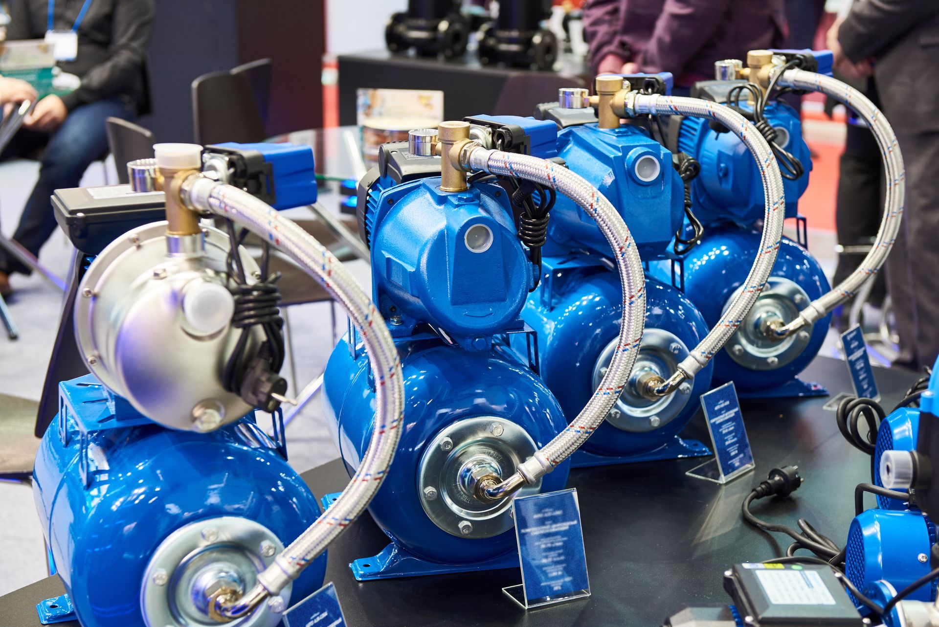 Blue water pumps on display at a trade show, connected by silver hoses.
