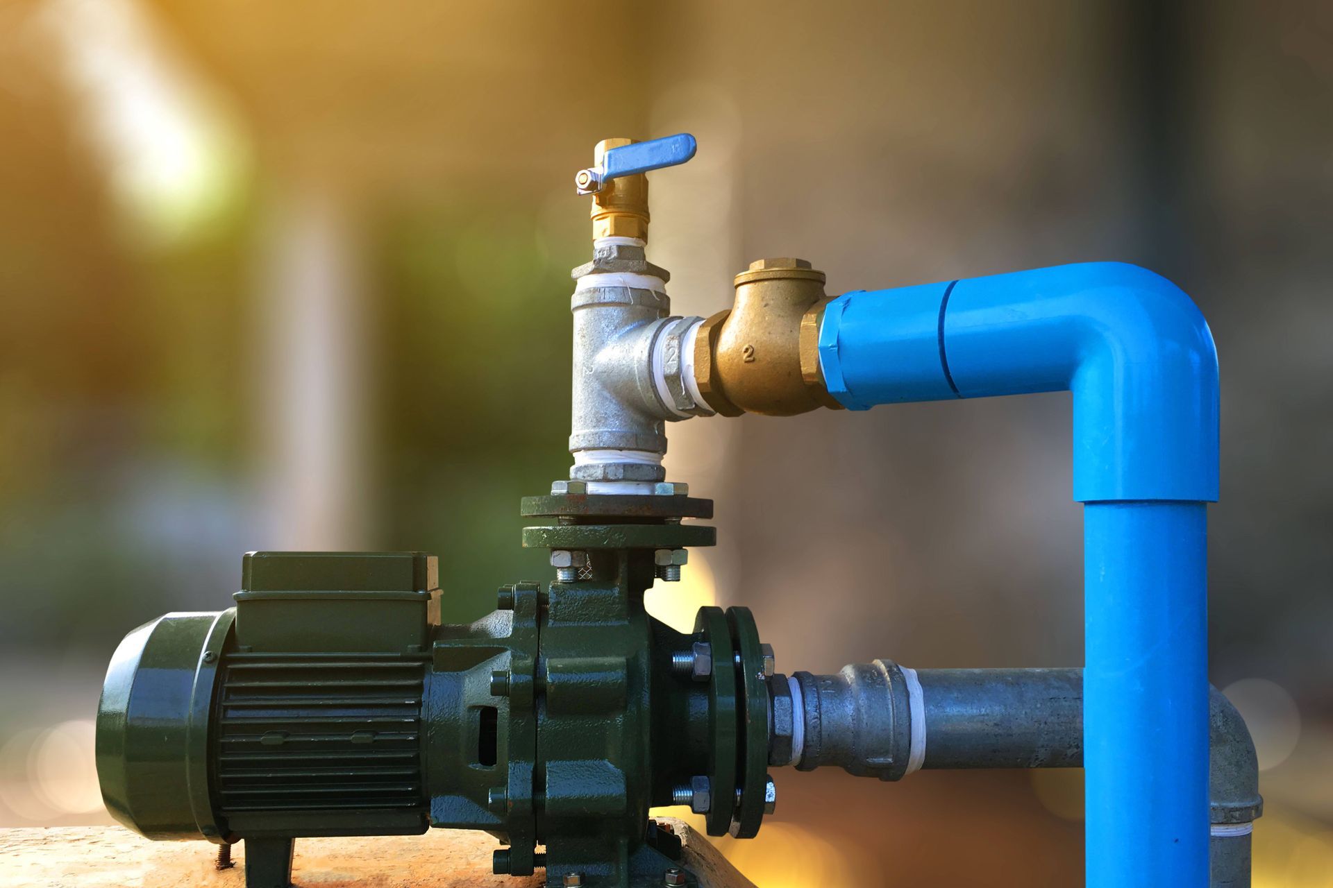 Water pump system connected to blue pipes with valve, shown in outdoor installation setting.