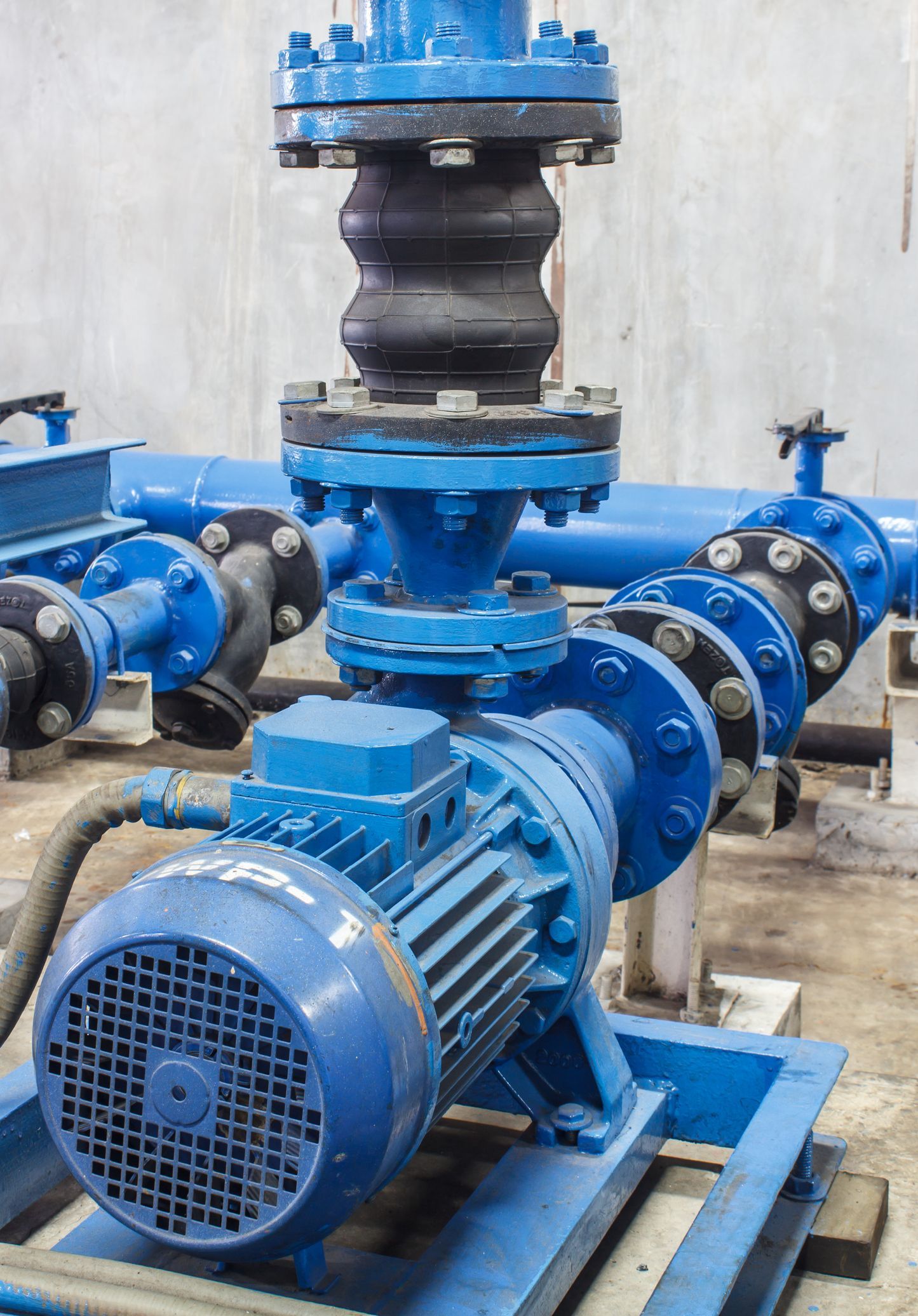 Blue industrial pump with pipes, fittings, and a flexible joint.