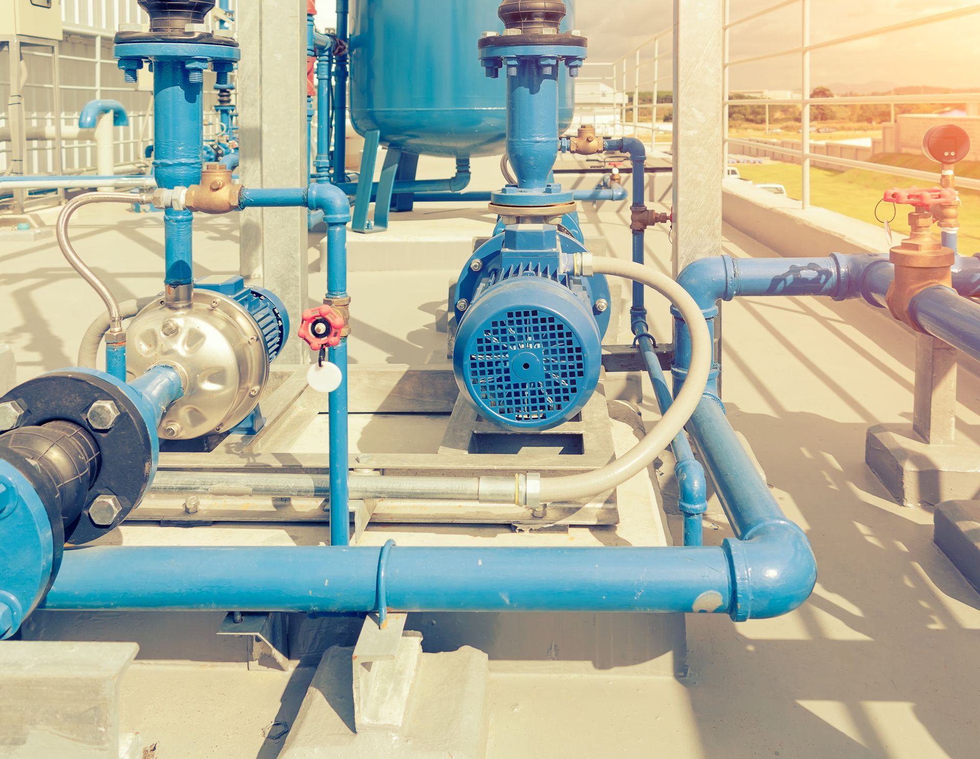 Blue industrial water pumps and pipes on a rooftop, with a bright sky in the background.