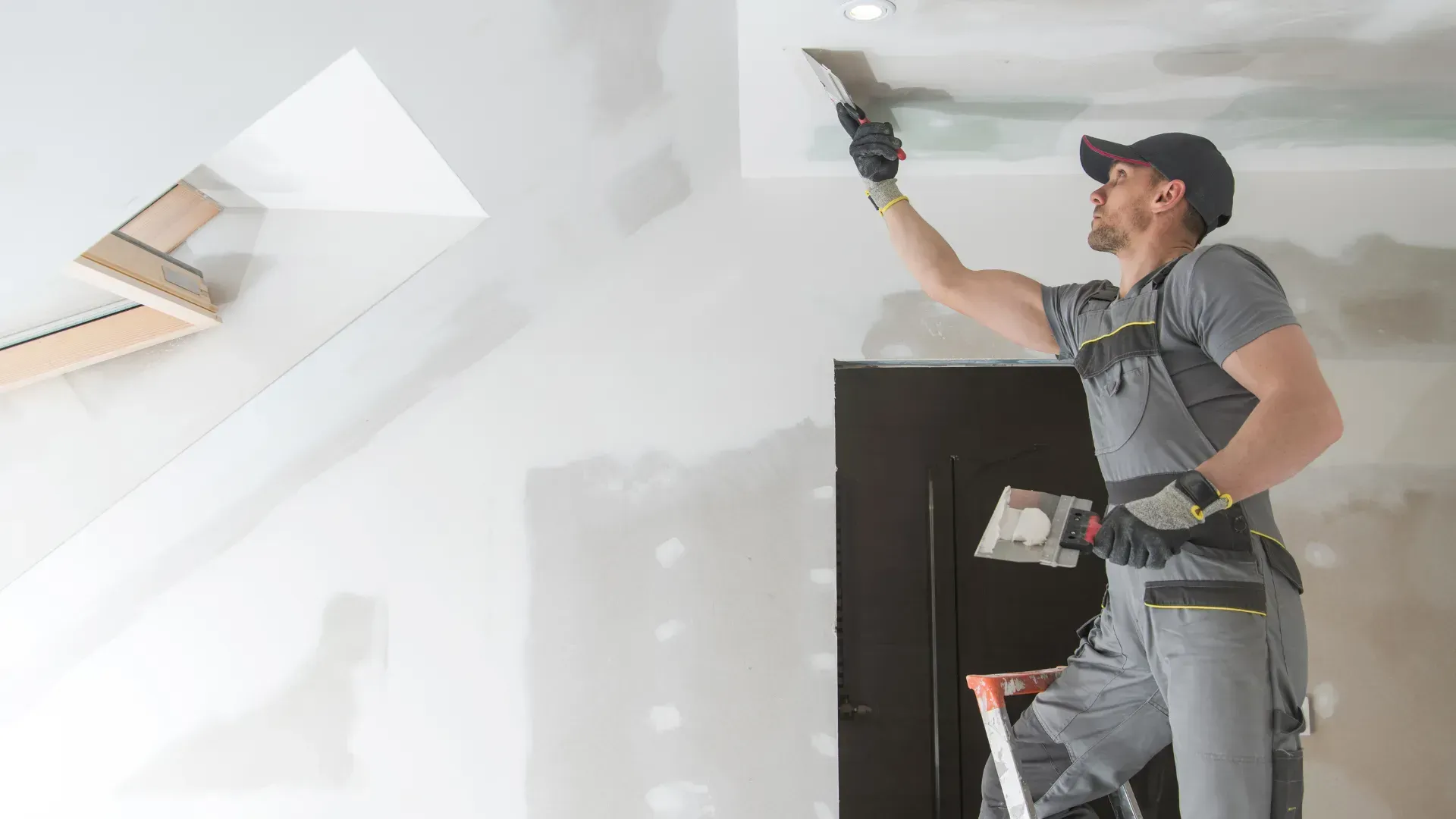 A man is standing on a ladder and plastering a ceiling.