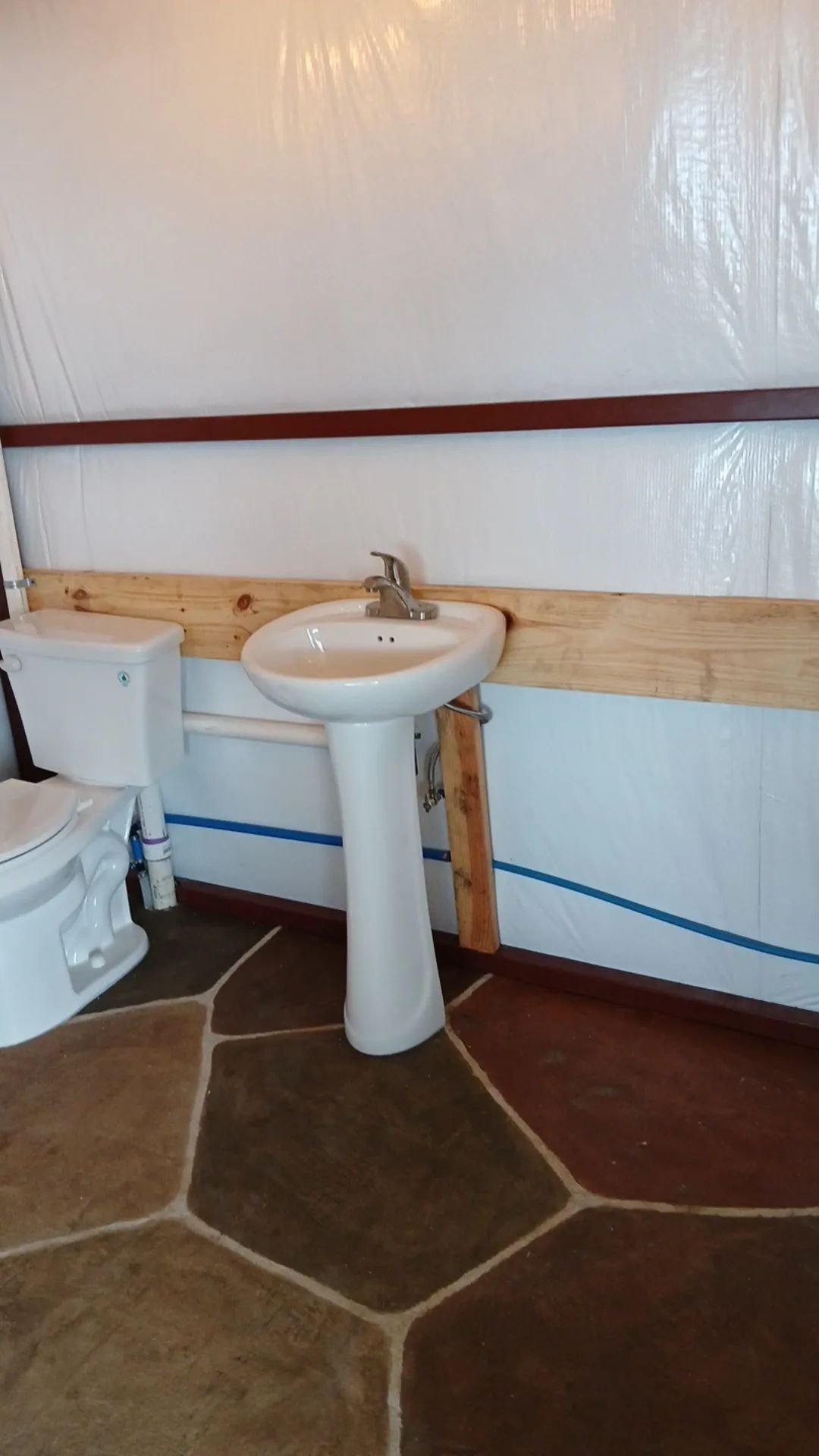 Bathroom with a pedestal sink, toilet, and stone tile floor. White walls and a brown wood beam.