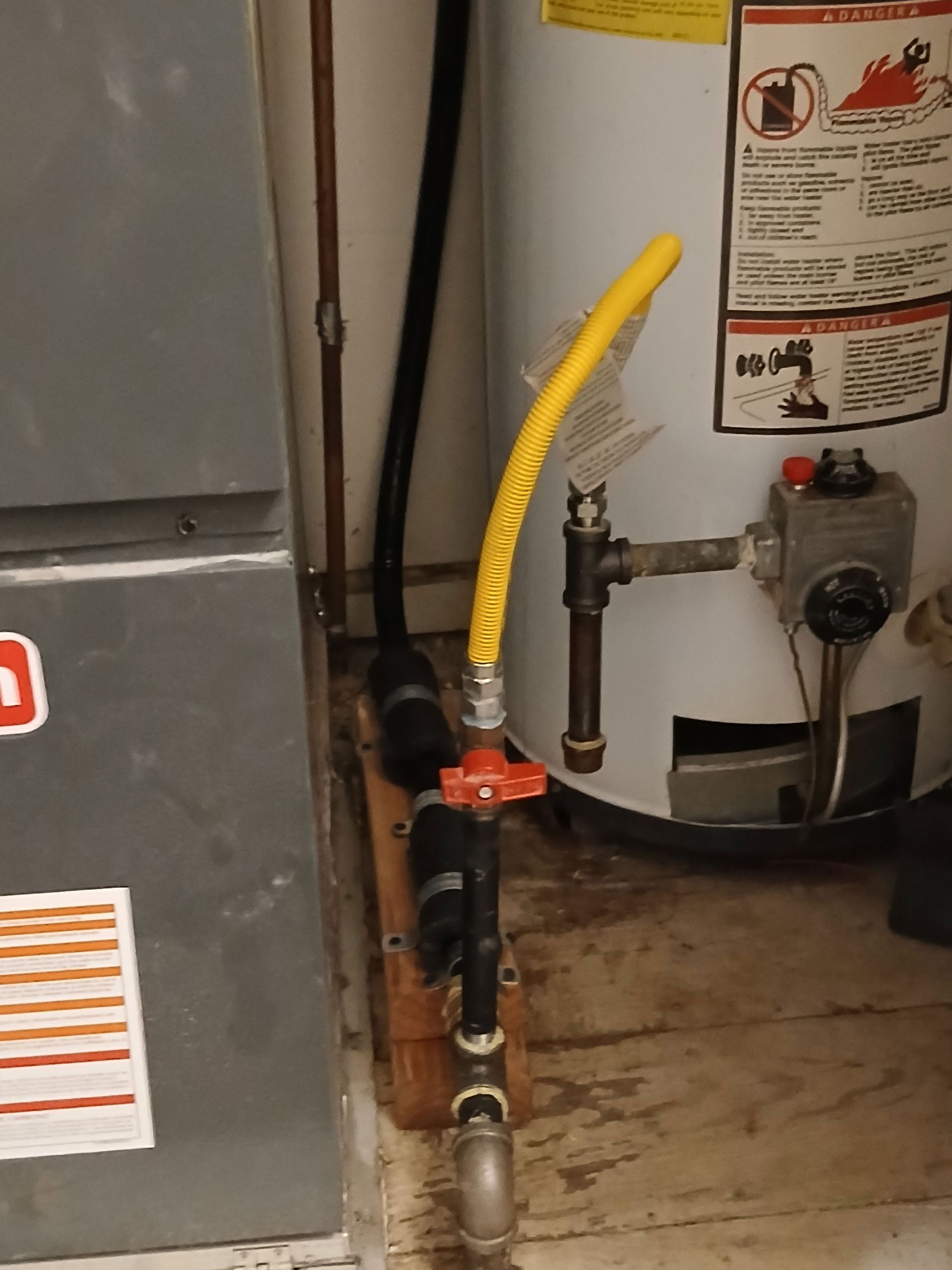 Gas shut-off valve and flexible yellow gas line connected to a water heater in a basement setting.