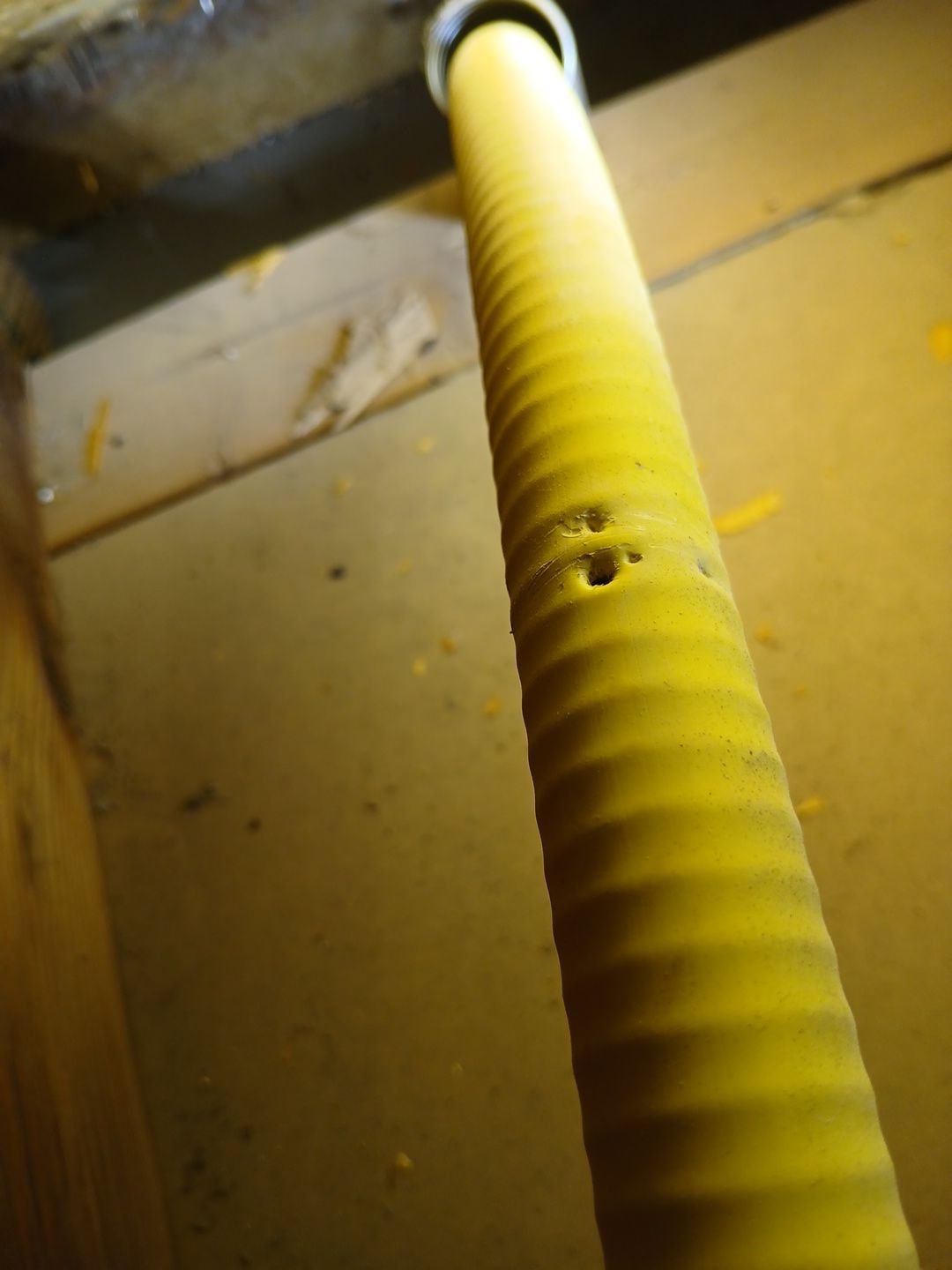 Yellow corrugated gas line with visible damage, holes in a wood-lined space.