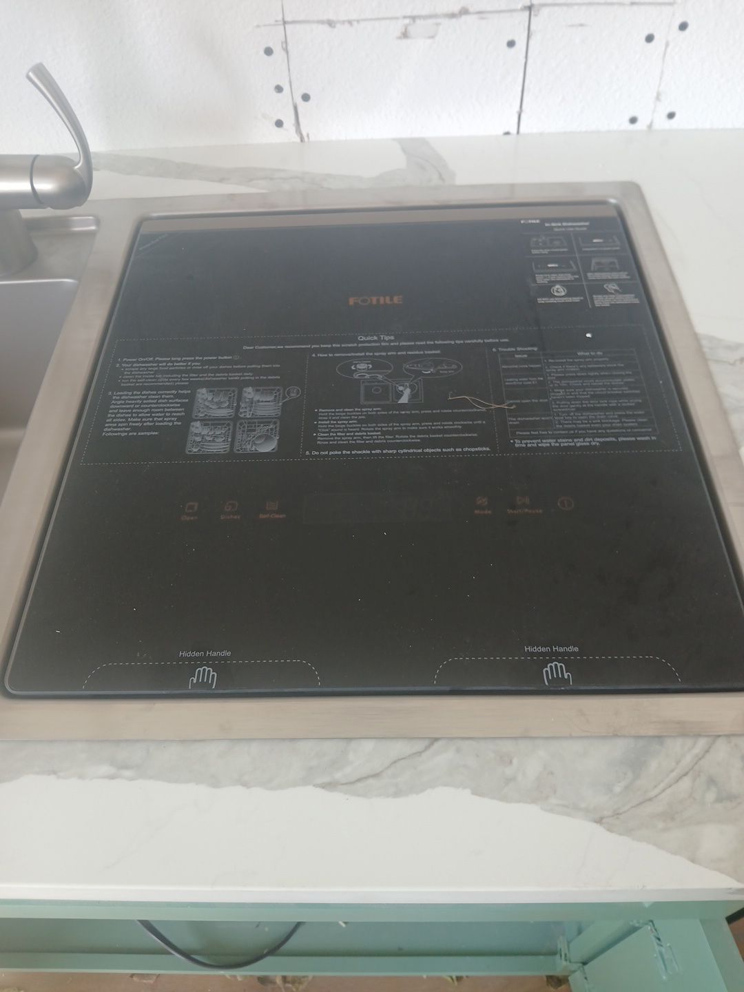 Black induction cooktop embedded in a marble countertop, near a kitchen faucet.