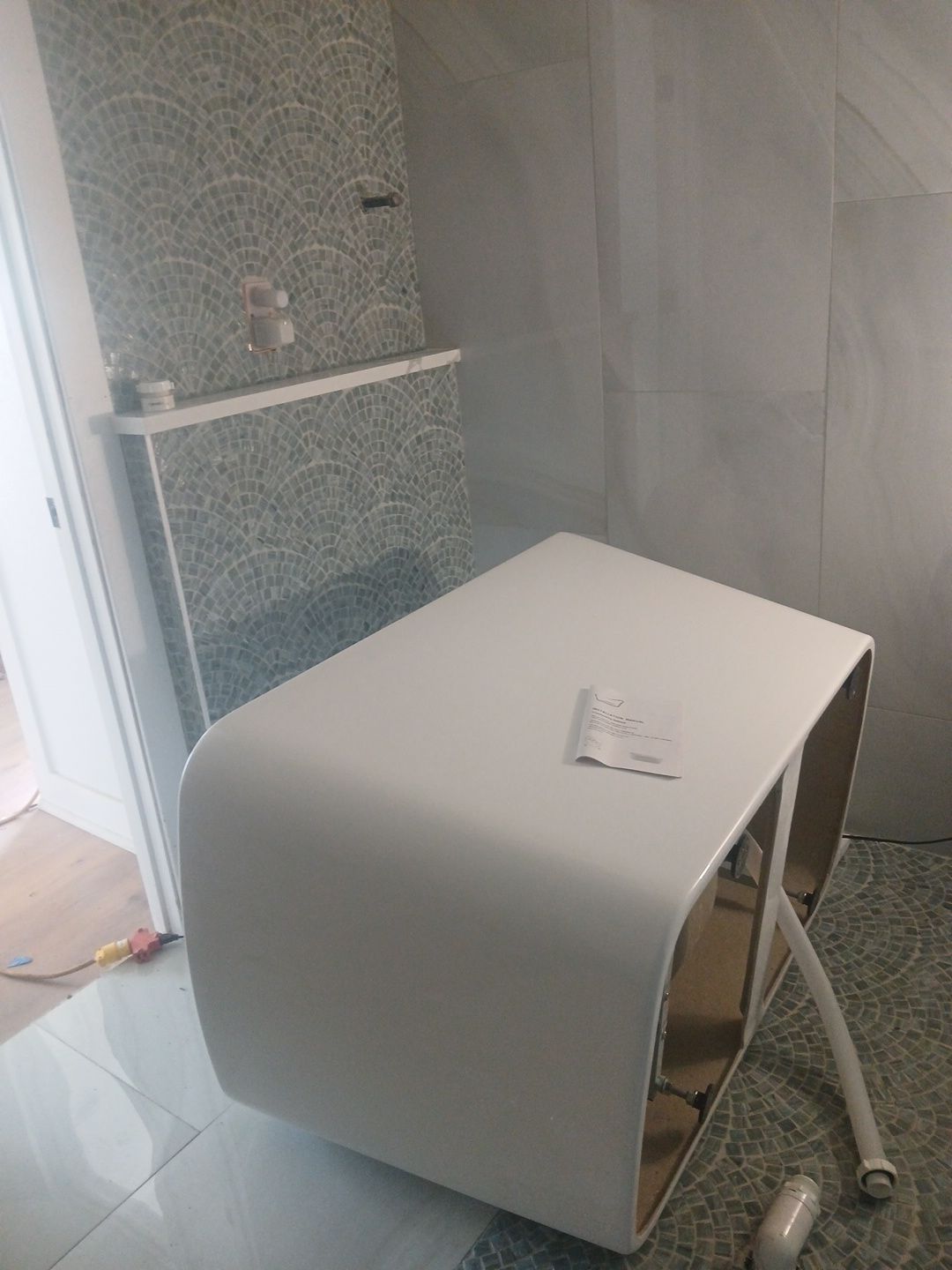 White, modern-shaped sink in a bathroom under construction, with textured wall and plumbing visible.