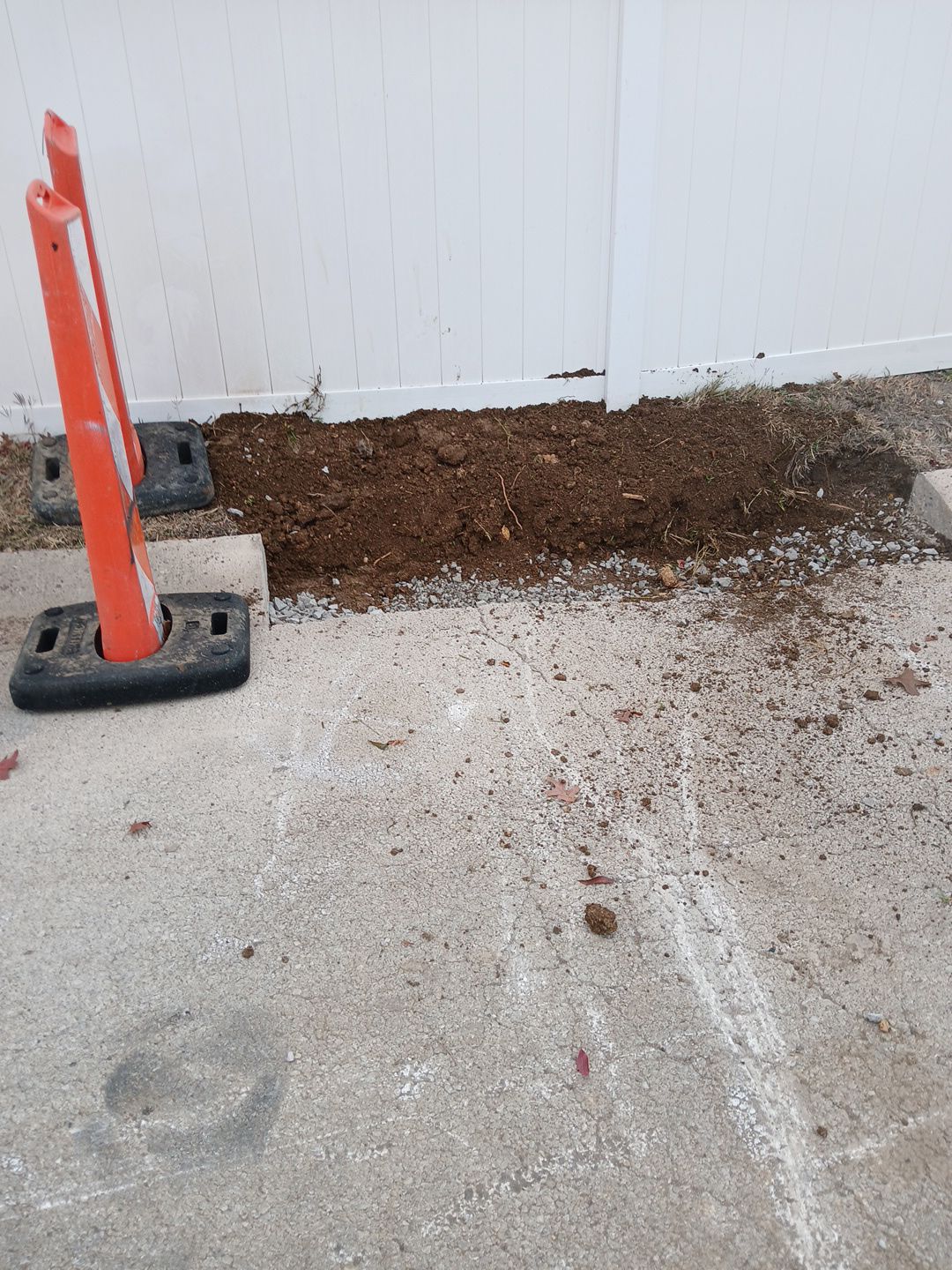 Orange traffic cones next to a dirt patch against a white wall and a concrete surface.