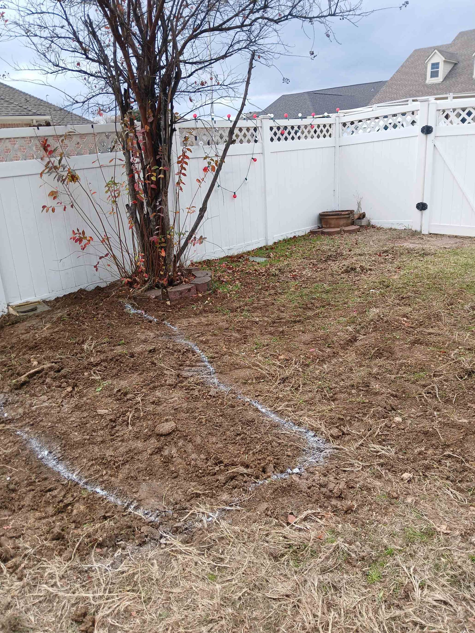 Yard with tree, white fence, and mulch marked with white lines.
