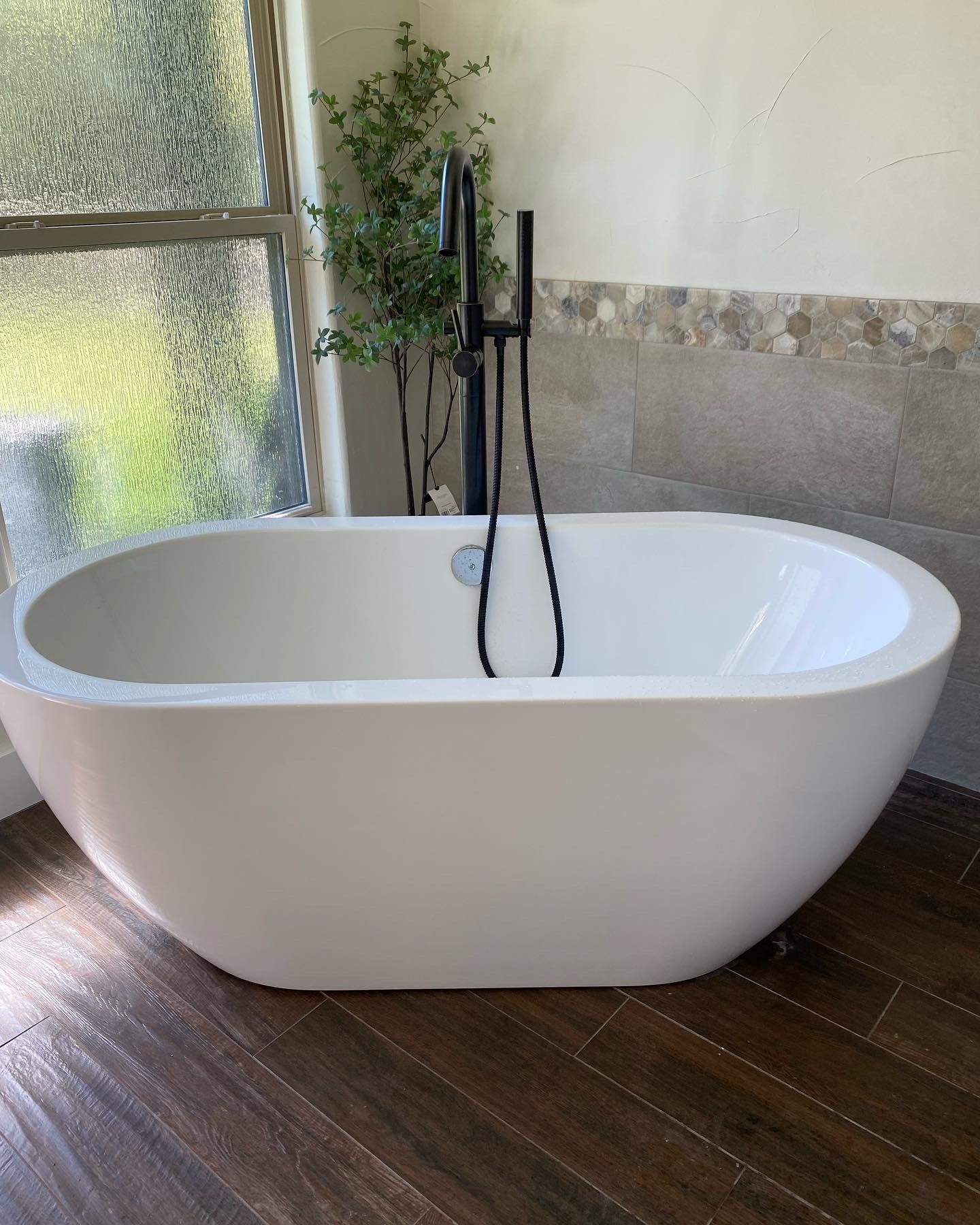 White oval bathtub with black faucet, by a window, in a modern bathroom.