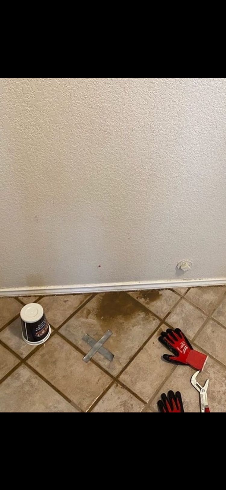 Messy floor with a spilled liquid, gloves, wrench, and a cup.