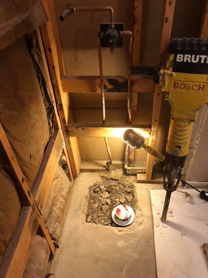 A construction site: exposed pipes, a jackhammer, and rubble within a wall cavity.