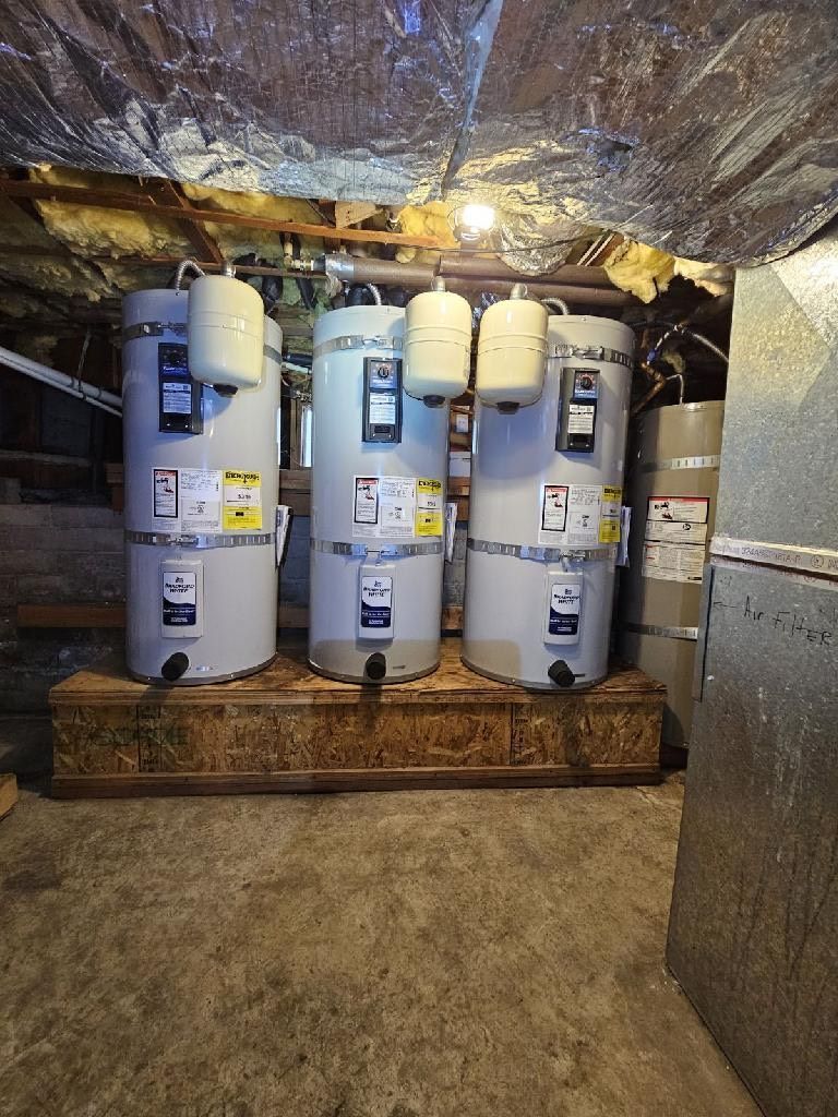 Three water heaters are sitting on top of a wooden box in a basement, Purist Plumbing and Excavation LLC