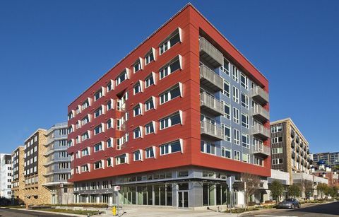 red and gray high-rise apartment building in urban setting with lower story retail in urban setting with blue sky