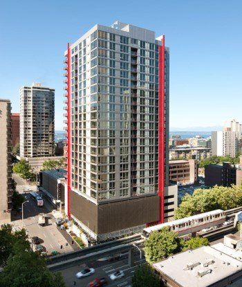 tall high–rise apartment building in urban setting with large glass windows and red accent panels with blue sky