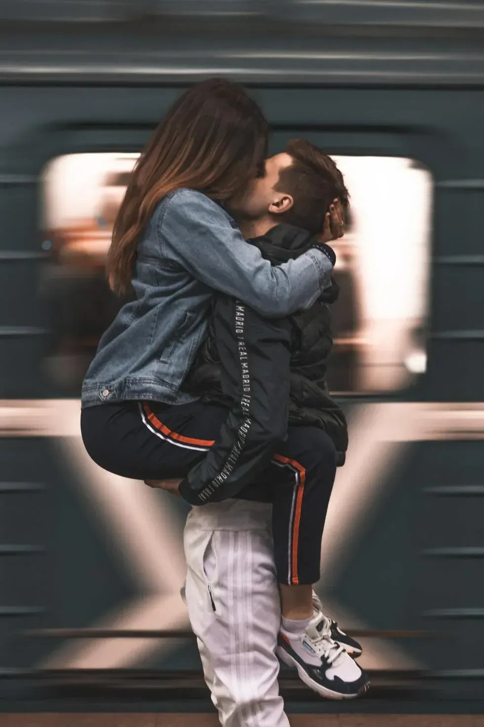 Couple kissing and embracing while one lifts the other in front of a blurred moving train