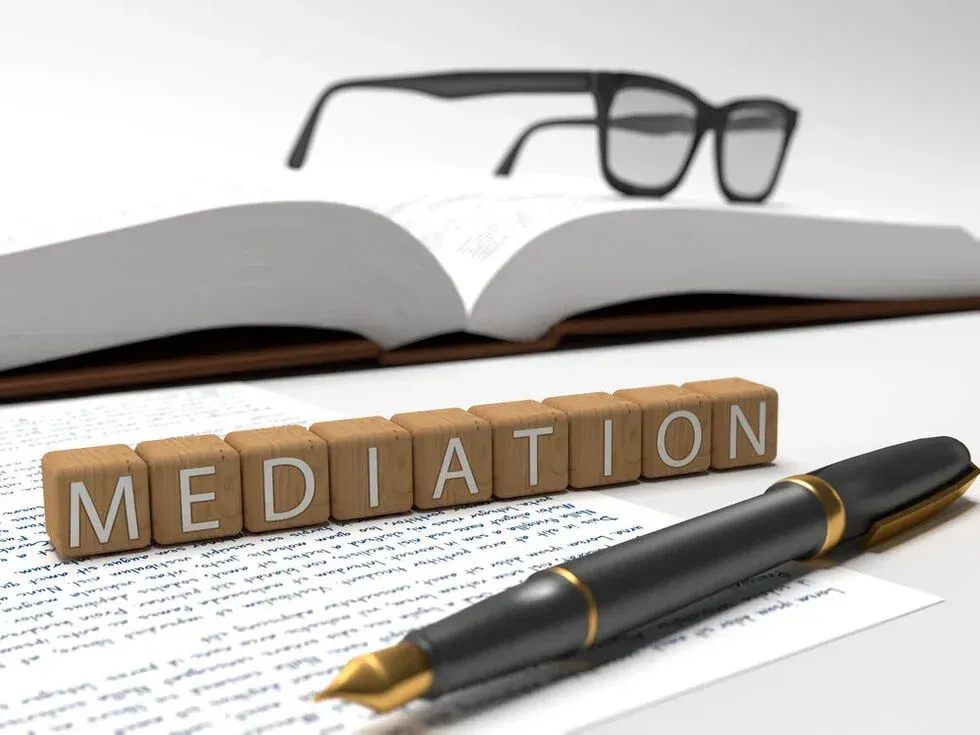 Open book, eyeglasses, and pen with wooden blocks spelling “MEDIATION”