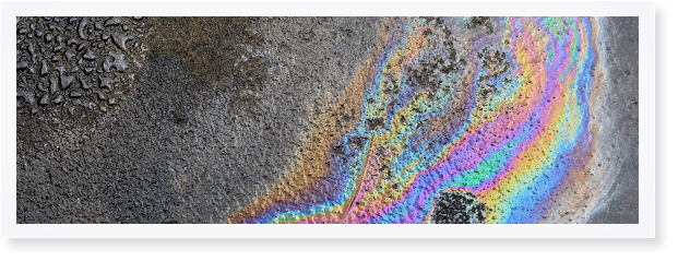 Een olievlek op een nat wegdek zorgt voor een glinsterende, regenboogkleurige reflectie.
