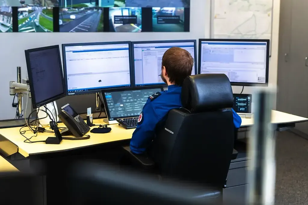 Ein Polizist sitzt an einem Schreibtisch vor drei Computermonitoren der Einsatzzentrale.