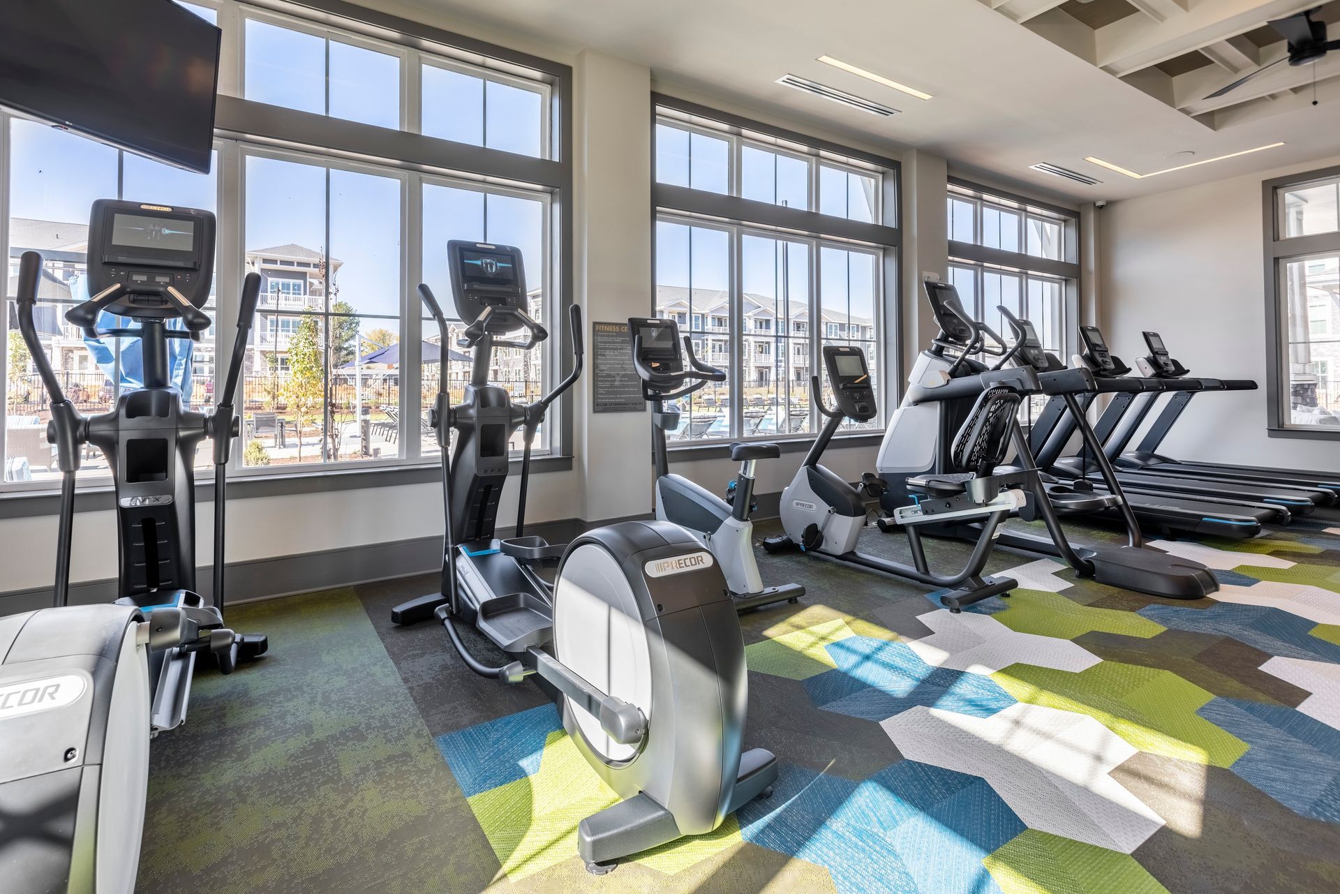 A gym with a lot of exercise equipment and a lot of windows.