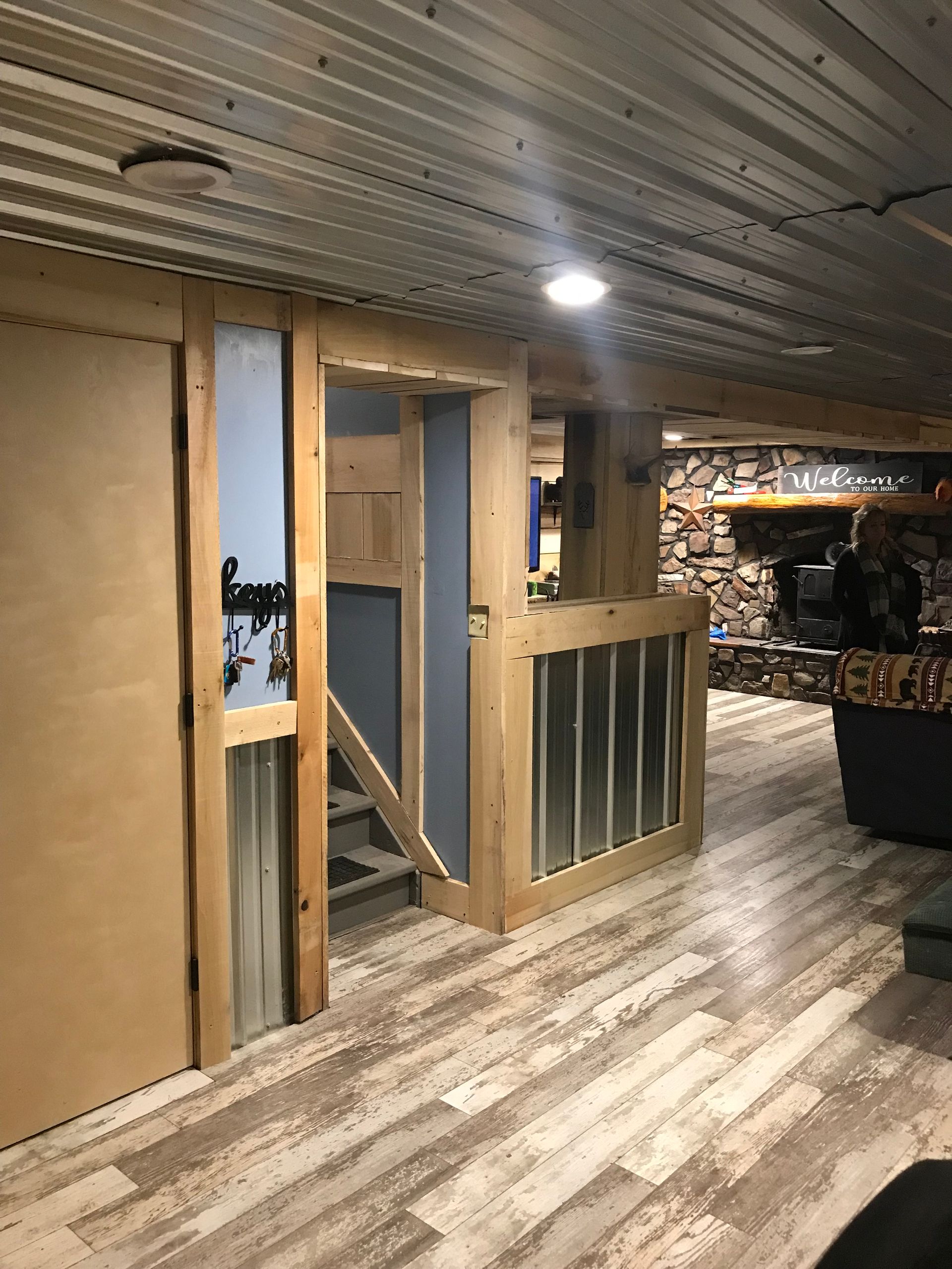 Rustic-style interior basement with wood-framed walls, corrugated metal accents, grey flooring, and a stairway entrance.