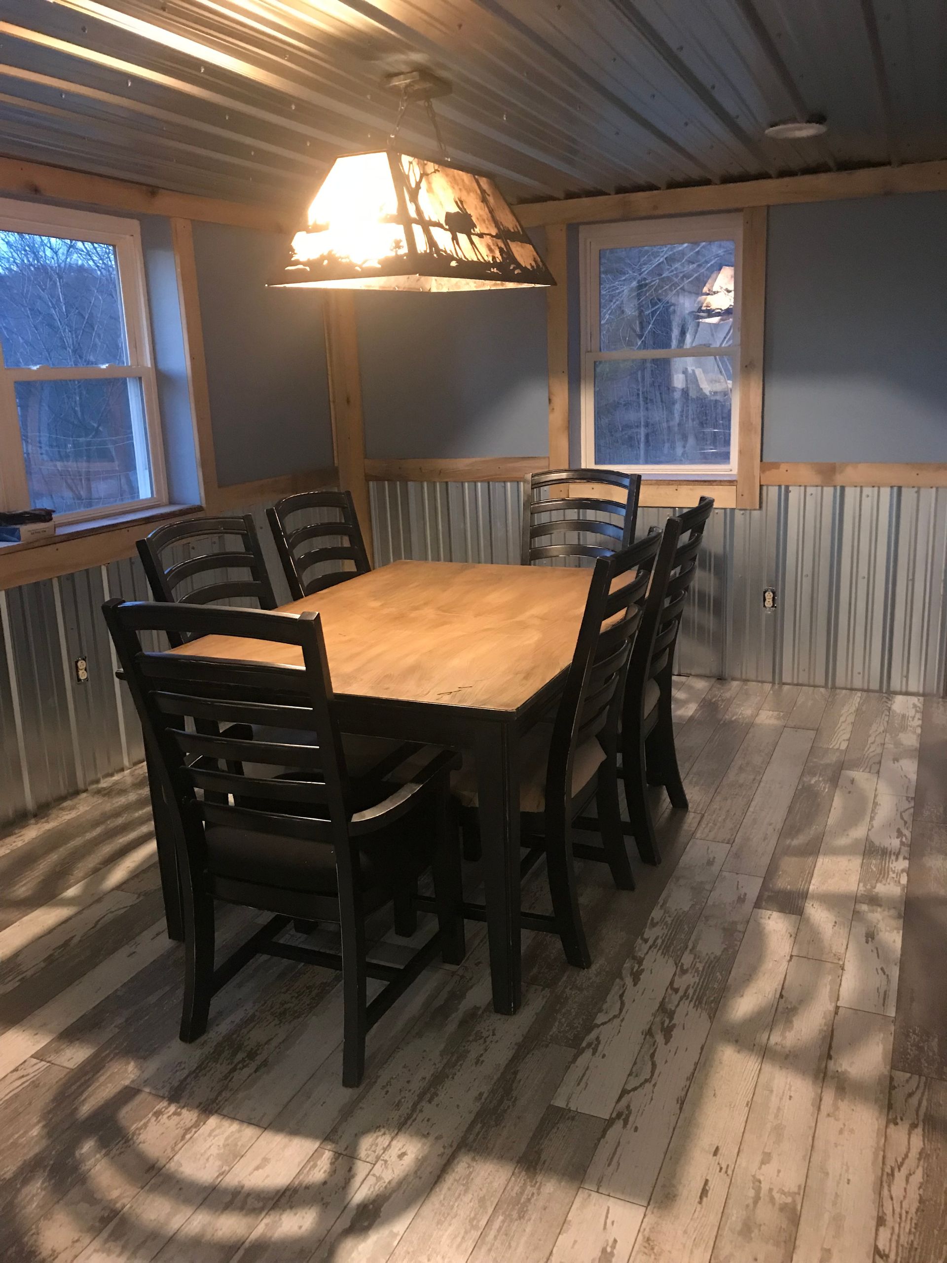 A dining room with a wooden table, dark chairs, rustic lighting, and walls paneled with corrugated metal.