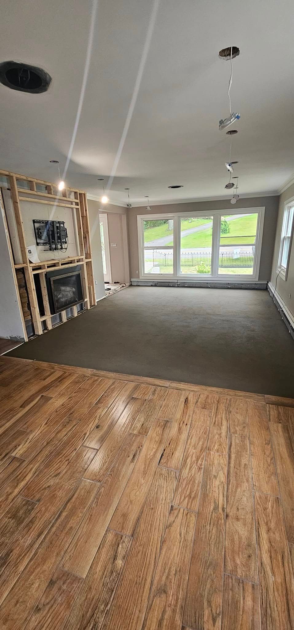 A renovated room with wood-look flooring, a gray carpeted area, and an unfinished fireplace framed in exposed wood studs.