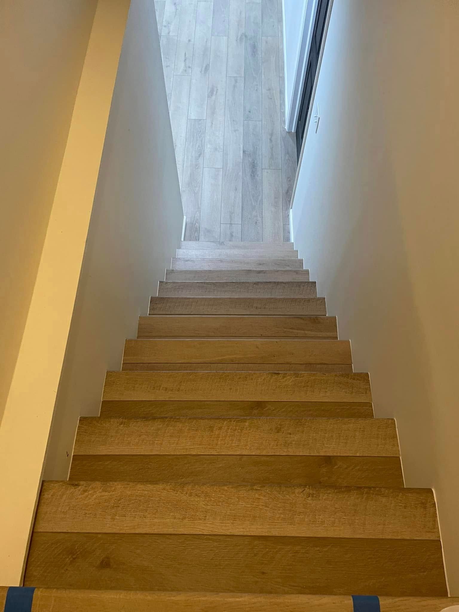 A low-angle view looking up a steep set of wooden stairs toward a bright, light-filled opening at the top.