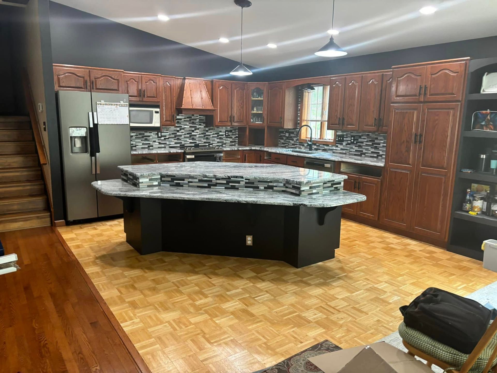 A modern kitchen features dark wood cabinets, granite countertops, a large center island, and tiled backsplash.