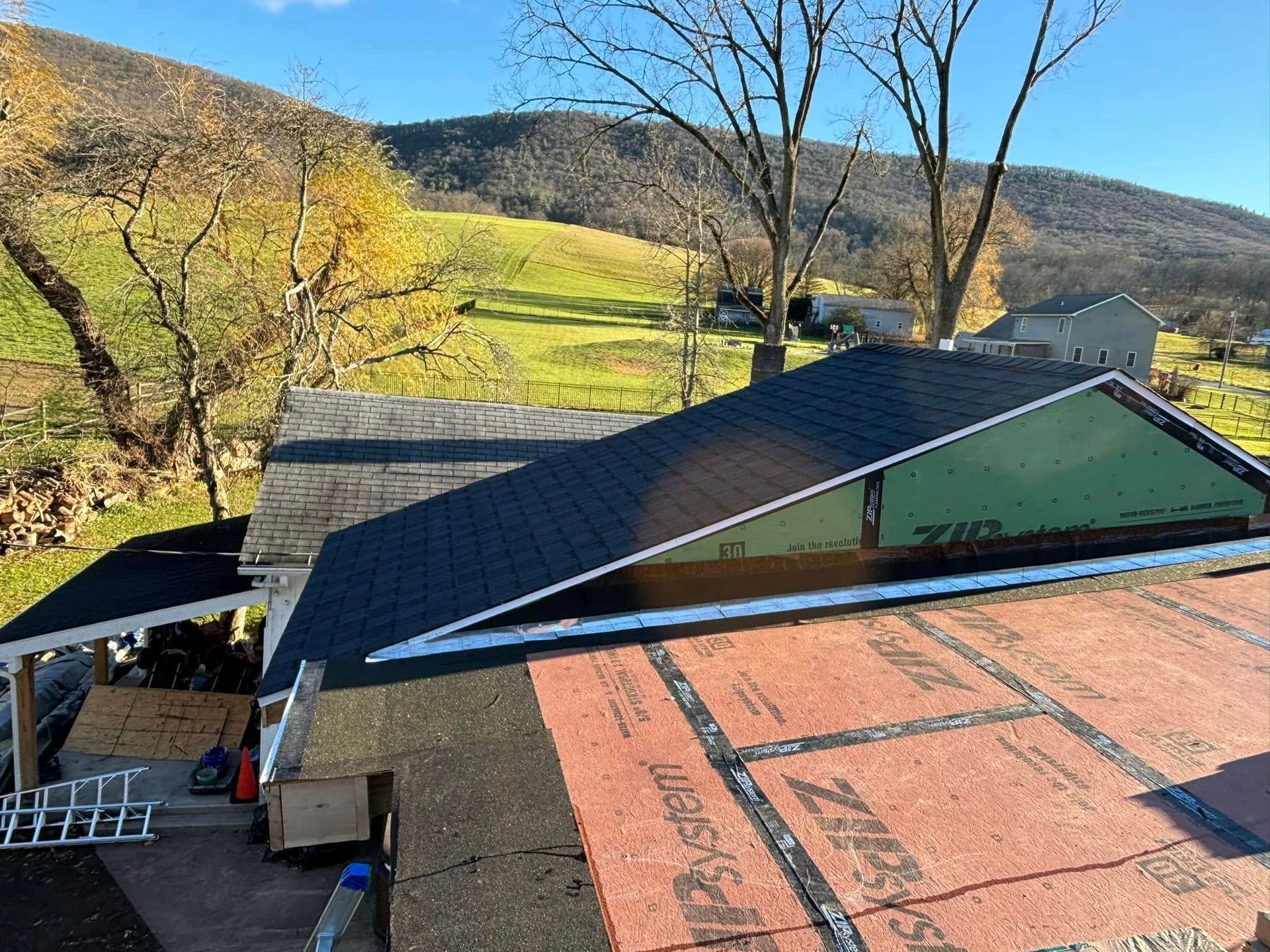 An aerial view of a house undergoing roof renovations, showing sections with new black shingles and bare underlayment.