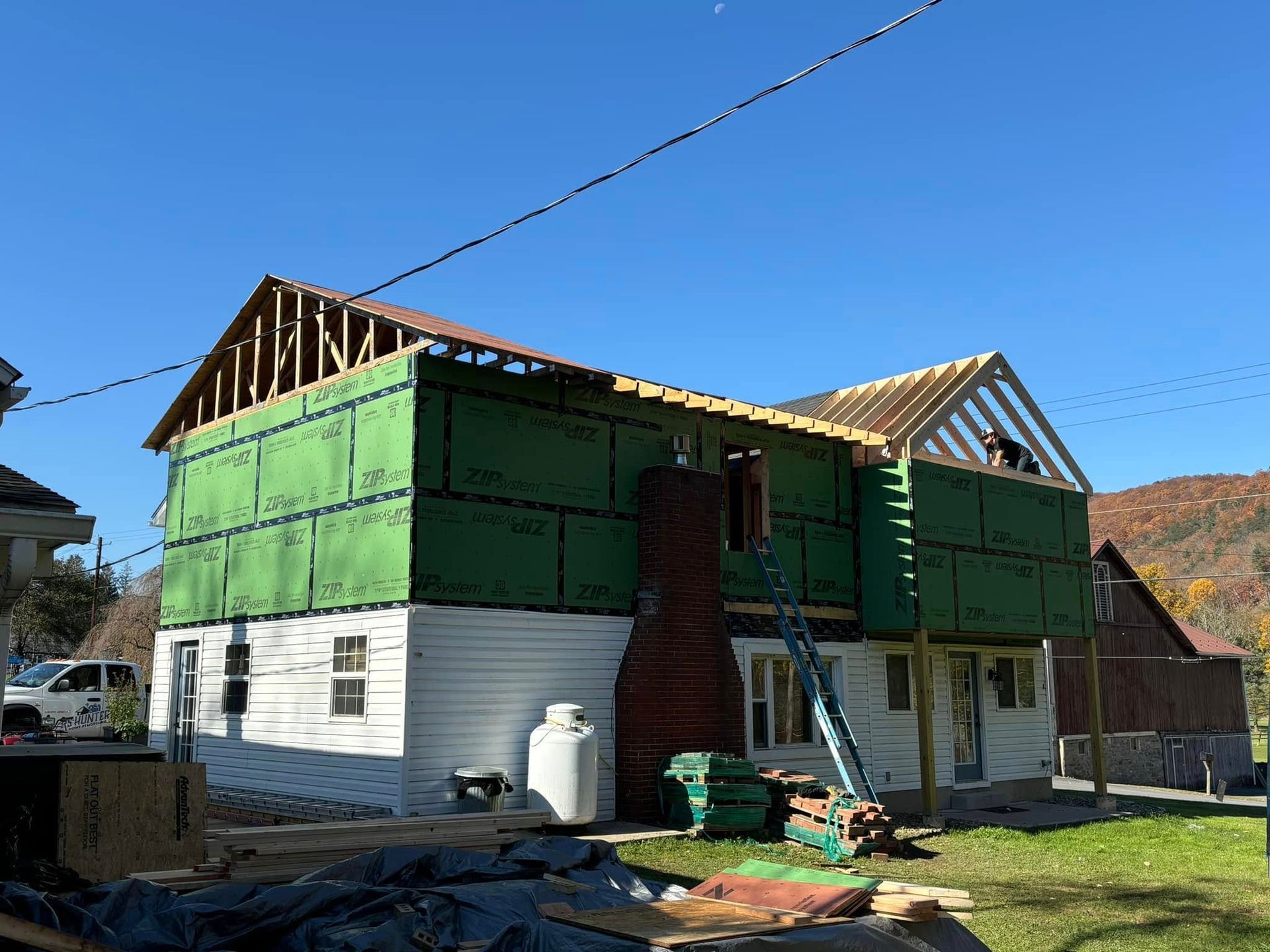 A brick ranch-style house with a covered porch, green lawn, and a damaged section of exterior siding on a cloudy day.